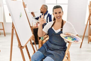 Sticker - Young artist woman at art studio doing ok sign with fingers, smiling friendly gesturing excellent symbol