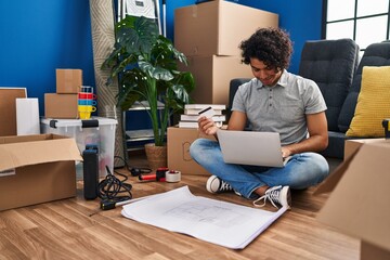 Sticker - Young hispanic man using laptop and credit card sitting on floor at new home