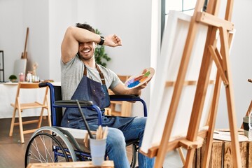 Sticker - Young hispanic man sitting on wheelchair painting at art studio smiling cheerful playing peek a boo with hands showing face. surprised and exited