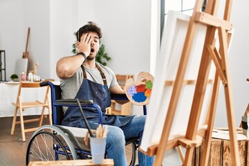 Poster - Young hispanic man sitting on wheelchair painting at art studio yawning tired covering half face, eye and mouth with hand. face hurts in pain.