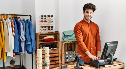 Young hispanic shopkeeper man smiling happy working at clothing store.