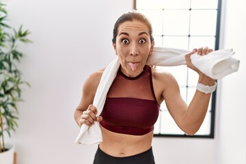 Sticker - Young hispanic woman wearing sportswear and towel at sport center sticking tongue out happy with funny expression.