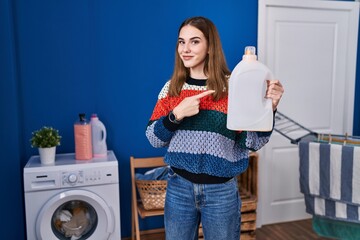 Canvas Print - Young hispanic girl holding detergent bottle smiling happy pointing with hand and finger