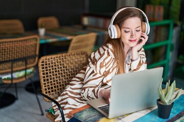 Canvas Print - Young caucasian woman using laptop and headphones sitting on table at restaurant