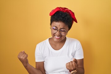 Sticker - Young african american woman standing over yellow background very happy and excited doing winner gesture with arms raised, smiling and screaming for success. celebration concept.