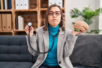 Sticker - Middle age hispanic woman working at therapy office holding brain puffing cheeks with funny face. mouth inflated with air, catching air.