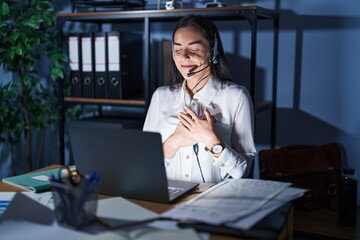 Poster - Young brunette woman wearing call center agent headset working late at night smiling with hands on chest with closed eyes and grateful gesture on face. health concept.