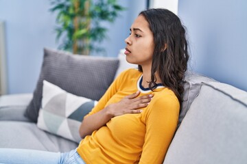 Wall Mural - Young african american woman stressed touching heart sitting on sofa at home