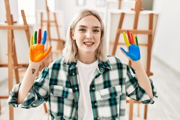 Wall Mural - Young artist student girl smiling happy showing colorful painted hands at art studio.