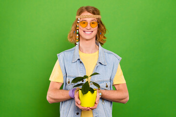 Poster - Portrait of attractive cheerful guy holding plant in hands growing isolated over bright green color background