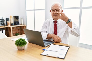 Wall Mural - Senior man working at the office using computer laptop pointing with hand finger to face and nose, smiling cheerful. beauty concept