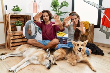 Sticker - Young hispanic couple doing laundry with dogs doing frame using hands palms and fingers, camera perspective