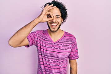 Wall Mural - Handsome hispanic man wearing casual pink t shirt doing ok gesture with hand smiling, eye looking through fingers with happy face.