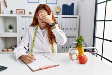 Wall Mural - Young redhead woman nutritionist doctor at the clinic covering eyes with hand, looking serious and sad. sightless, hiding and rejection concept