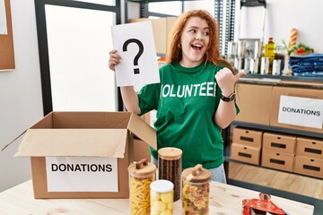 Canvas Print - Young redhead woman wearing volunteer t shirt holding question mark pointing thumb up to the side smiling happy with open mouth