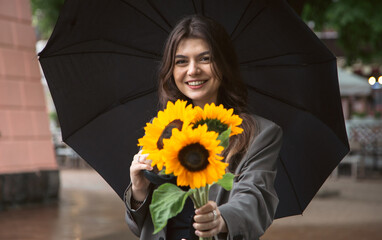 Wall Mural - A young woman with a bouquet of sunflowers under an umbrella in rainy weather.