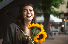 A Young Woman With A Bouquet Of Sunflowers Under An Umbrella In Rainy Weather.