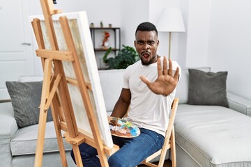 Wall Mural - Young african man painting on canvas at home doing stop gesture with hands palms, angry and frustration expression