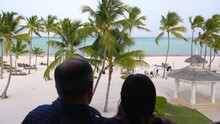 Husband And Wife Enjoying Beach Scenery From Balcony. Vacationing At Caribbean Resort. On Third Floor Overlooking White Sand And Ocean.