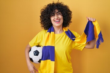 Sticker - Young brunette woman with curly hair football hooligan holding ball celebrating crazy and amazed for success with open eyes screaming excited.