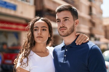 Young hispanic couple hugging each other standing with relaxed expression at street