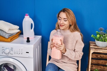 Wall Mural - Young woman smelling detergent waiting for washing machine at laundry room