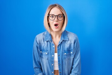 Sticker - Young caucasian woman standing over blue background afraid and shocked with surprise expression, fear and excited face.