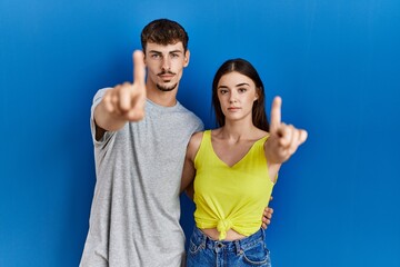 Sticker - Young hispanic couple standing together over blue background pointing with finger up and angry expression, showing no gesture