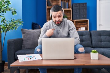 Wall Mural - Hispanic man using laptop working from home pointing finger to one self smiling happy and proud