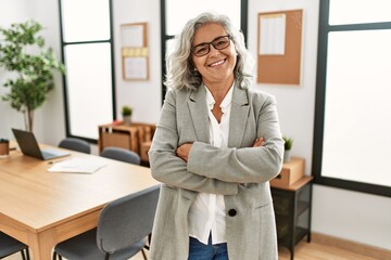 middle age grey-haired businesswoman smiling happy standing with arms crossed gesture at the office.