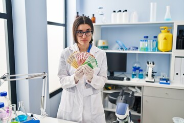 Poster - Young hispanic woman working at scientist laboratory holding money banknotes depressed and worry for distress, crying angry and afraid. sad expression.