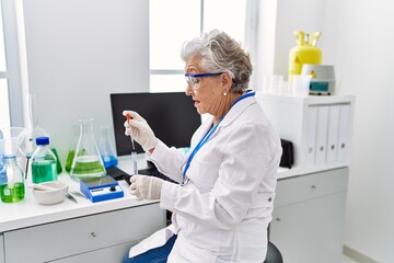 Wall Mural - Senior grey-haired woman wearing scientist uniform using pipette and test tube at laboratory