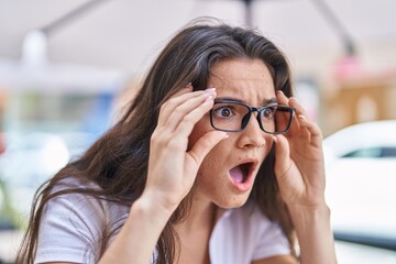 Young hispanic woman wearing glasses standing with surprise expression at street