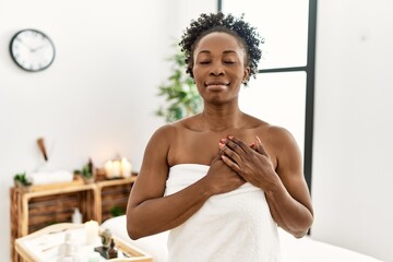 Wall Mural - Young african american woman wearing towel standing at beauty center smiling with hands on chest with closed eyes and grateful gesture on face. health concept.