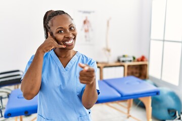 Wall Mural - Black woman with braids working at pain recovery clinic smiling doing talking on the telephone gesture and pointing to you. call me.