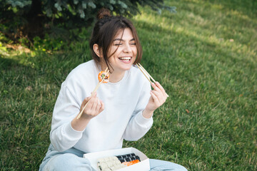 Wall Mural - A young woman eating sushi in the park, picnic in nature.