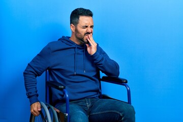 Poster - Handsome hispanic man with beard sitting on wheelchair touching mouth with hand with painful expression because of toothache or dental illness on teeth. dentist