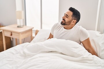 Sticker - Young hispanic man smiling confident sitting on bed at bedroom