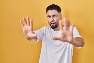 Poster - Young handsome man wearing casual t shirt over yellow background afraid and terrified with fear expression stop gesture with hands, shouting in shock. panic concept.