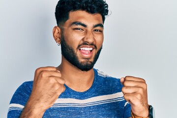 Wall Mural - Arab man with beard wearing casual striped t shirt screaming proud, celebrating victory and success very excited with raised arms