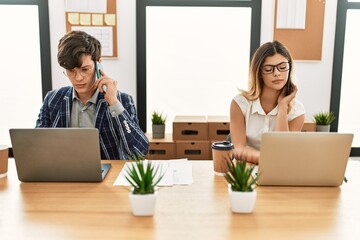 Wall Mural - Two business workers with serious expression working using smartphone and laptop at the office.