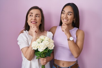 Poster - Hispanic mother and daughter holding bouquet of white flowers with hand on chin thinking about question, pensive expression. smiling and thoughtful face. doubt concept.