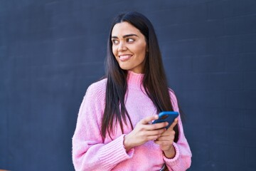 Wall Mural - Young hispanic woman smiling confident using smartphone at street