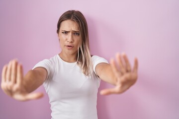 Sticker - Blonde caucasian woman standing over pink background doing stop gesture with hands palms, angry and frustration expression