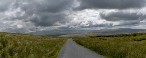 Poster - panorama landscape of County Donegal under an overcast sky with a small country road leading to the horizon