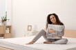 © New Africa - Happy young African American woman hugging pillow on bed with comfortable mattress at home