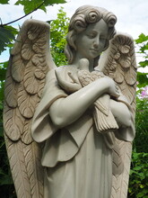 An Angel With A Dove. Sculpture In The Cemetery. The Figure Of An Angel With Wings Holding A Bird In His Arms. Lamentation For The Deceased. Headstone Monument On A Christian Grave. Sadness And Sorrow