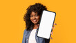 © Prostock-studio - Cheerful black woman showing cell phone on yellow, mockup