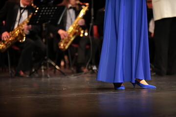 Wall Mural - A woman in a blue long dress stands on stage performing with a brass jazz orchestra festive clothes of the artist to the floor