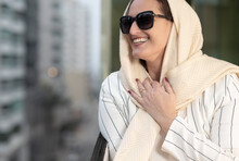 Classic Beauty Caucasian Woman Wearing Elegant Clothes With A Scarf And Sunglasses Smiling In An Urban Environment Amid Buildings.